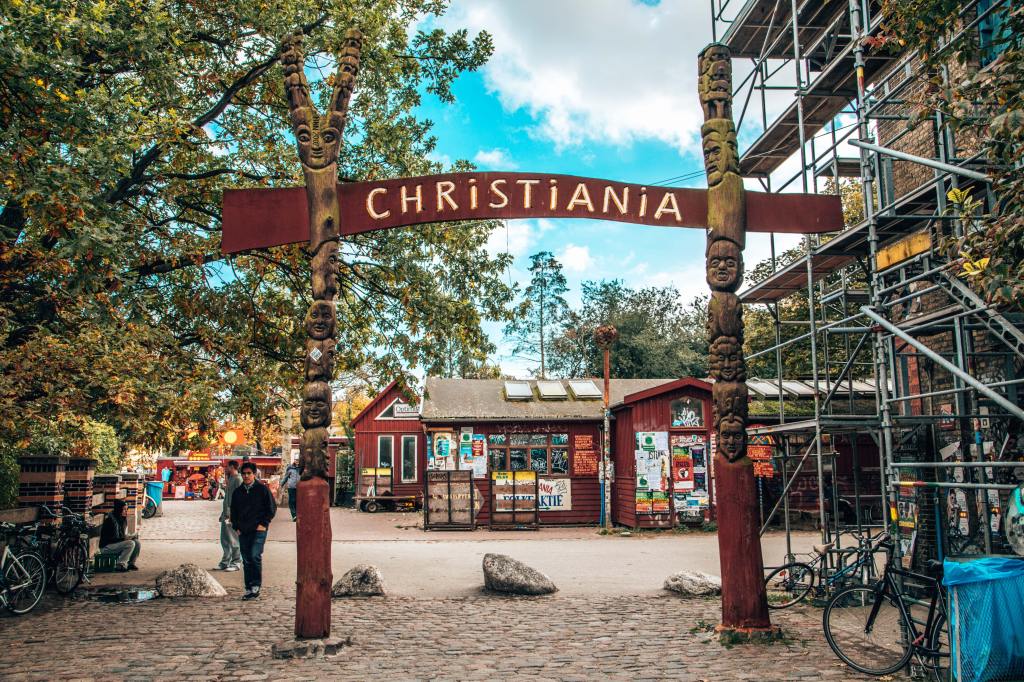 handmade totem sign saying 'Christiania' on a cobblestone street in front of a wooden cabin